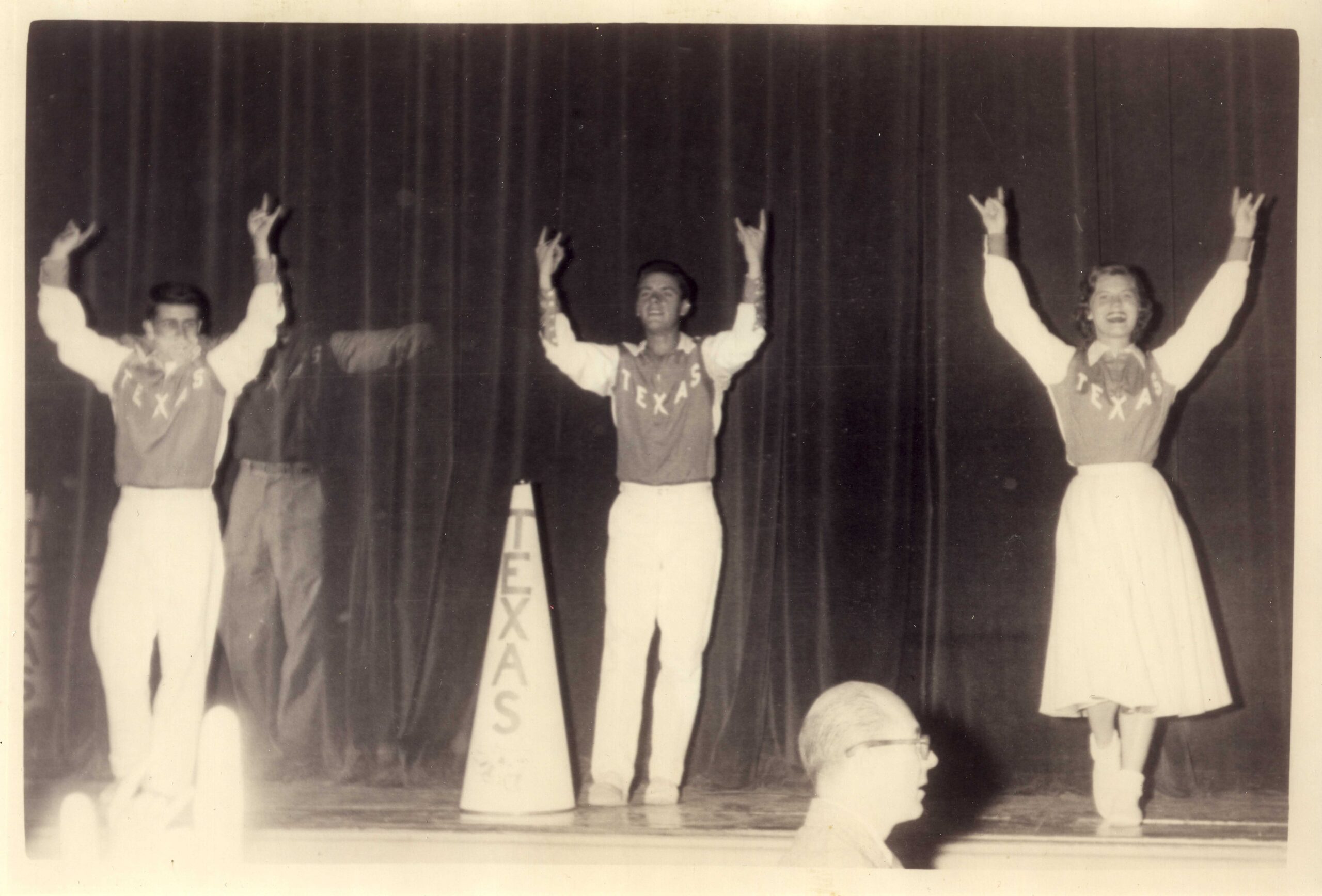 Cheerleaders on stage hold up the Hook 'Em Horns hand signal